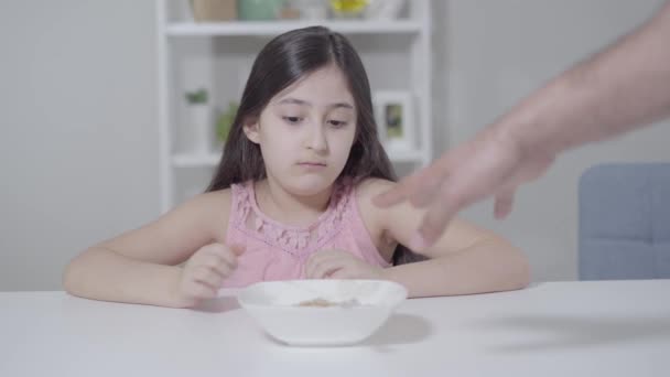 Oigenkännlig far ger tallrik med havregryn till dottern på morgonen. Söt Mellanösterntjej som äter frukost hemma. Hälsosam kost, kost, näring, vård. — Stockvideo