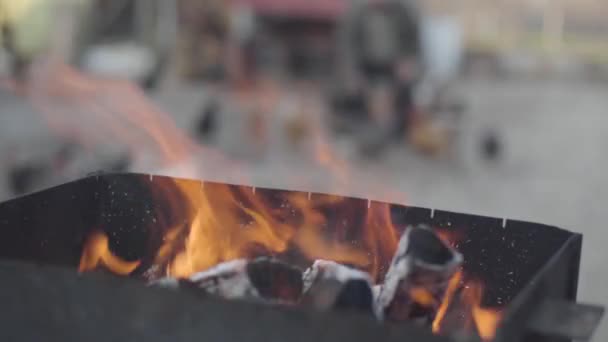 Detailní záběr rudého plamene hořícího v grilu grilu, jak stará rozmazaná běloška krmí v pozadí kuře. Vaření, grilování, venkovský životní styl. — Stock video