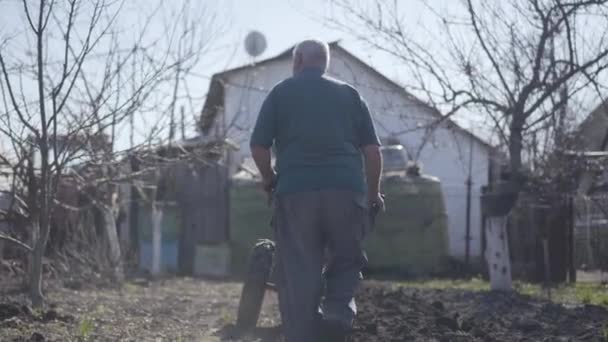 Vue arrière de l'homme caucasien mature applaudissant les mains comme sol fertile sillonnant au début du printemps. Fermier senior travaillant dans un jardin rural et utilisant de l'équipement pour la fabrication de sillons. Agriculture, culture . — Video
