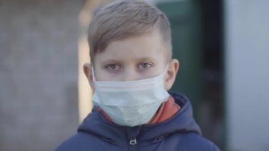 Covid-19 karantinasının sonunda beyaz bir çocuğun maskesini çıkarmasının portresi. Kameraya bakıp gülümseyen sağlıklı bir çocuk. Salgın, küresel tehlike, güvenlik önlemleri.
