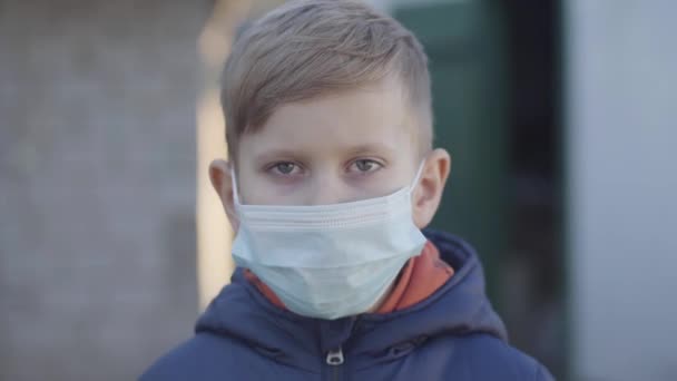 Portrait d'un petit garçon caucasien enlevant un masque facial à la fin de la quarantaine de Covid-19. Heureux enfant en bonne santé regardant la caméra et souriant. Pandémie, risque mondial, mesures de sécurité . — Video