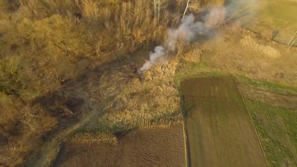 Vista aérea de agricultores quemando fuego en el campo. La gente incinera hojas y ramas secas a principios de primavera. Agricultura, daños medioambientales, contaminación . — Vídeos de Stock