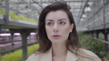 Glasshouse 'da duran güzel esmer, beyaz bir kadının yakın plan yüzü. Seradaki bitkilerin arka planında büyüleyici gizemli kadının portresi.