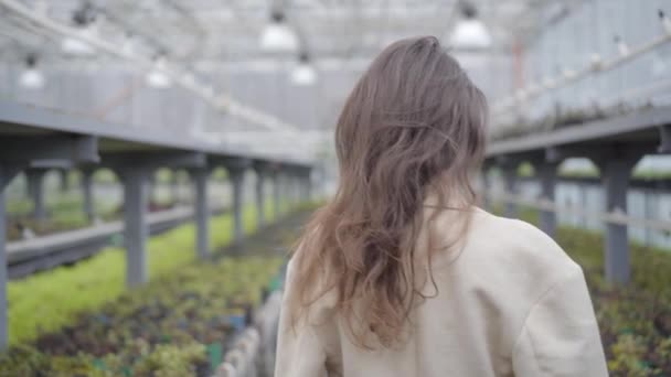 Ung brunett vit kvinna vänder sig till kameran som stående i växthus. Enigmatisk dam med bruna ögon poserar i växthuset. — Stockvideo