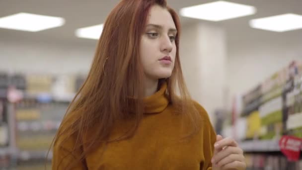 Portrait of focused redhead Caucasian woman with green eyes shopping in wine shop. Confident gorgeous girl choosing alcohol drink in supermarket. Lifestyle, buying, purchasing. — Stock Video