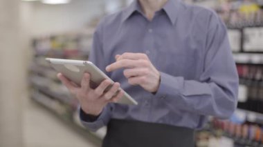 Markette bulanık rafların arkasında tablet kullanan tanımlanamayan yetişkin bir beyaz adam. Erkek müşteri, modern kablosuz teknolojileri kullanarak içeceğin doğruluğunu onaylıyor..