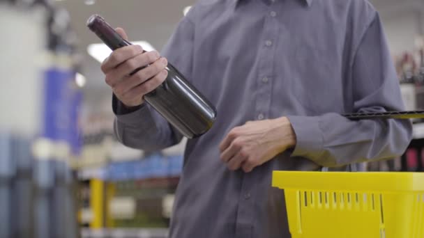 Männliche kaukasische Hand hält Flasche Rotwein in Alkohol Supermarkt. Unbekannter erwachsener Mann legt Getränk in gelben Einkaufskorb Unternehmen, Konsum, Lebensstil, Freizeit. — Stockvideo