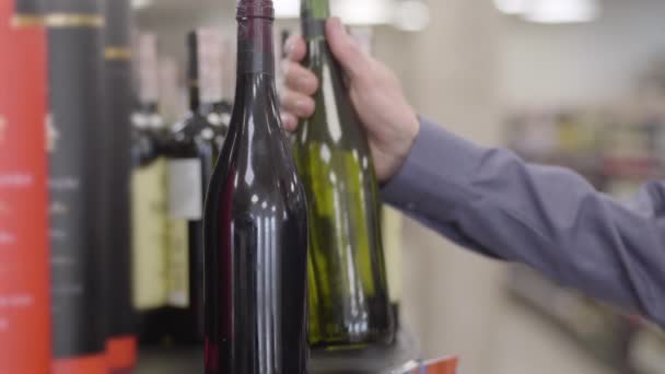 Male Caucasian hand taking bottle of white wine on the shelf. Blurred adult man leaving walking along shelves in alcohol shop. Leisure, lifestyle, weekends, beverage. — Stock Video