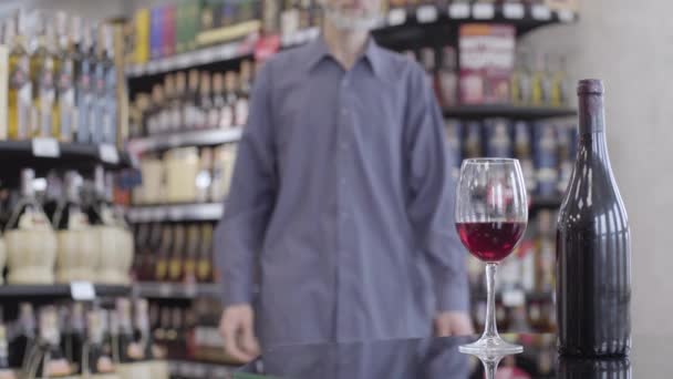 Hombre caucásico irreconocible tomando vino de la mesa y batiendo la bebida en vidrio. Cliente masculino degustando costosa bebida de lujo en el supermercado de alcohol. Estilo de vida, compras, elección . — Vídeo de stock