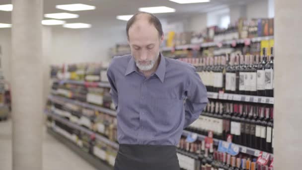 Een slanke blanke man die een zwart schort draagt en handen kruist in een slijterij. Portret van ervaren sommelier die poseert in de supermarkt. Beroep, levensstijl, perfectie, alcohol. — Stockvideo