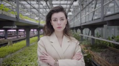 Cam evde elleri çapraz duran güzel beyaz bir kadın. Seradaki çekici genç bayanın yüzüne kamera yaklaşıyor..