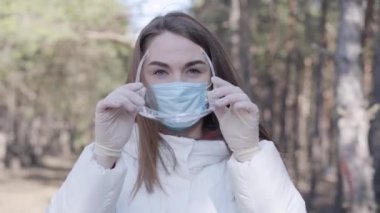 Koruyucu eldivenler ve yüz maskesi takan şeffaf gözlük takan ciddi bir beyaz kız. Koronavirüs karantinası sırasında dışarıda dinlenirken kendine güvenen genç bir kadın. Covid 19.
