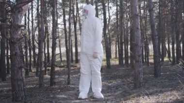 Kenar mahalle yolunun yanındaki ormanda duran beyaz takım elbiseli, bilinci açık, beyaz, genç bir adam. Alnından başka yere bakıyor. Koronavirüs karantinasının kontrolü uyumu ölçer. Geniş açı.
