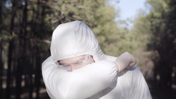 Портрет молодого человека в защитном костюме, чихающего или кашляющего и показывающего большой палец вверх. Кавказский вирусолог в маске на открытом воздухе на карантине Ковид-19. Симптомы коронавируса, инфекционные заболевания . — стоковое видео