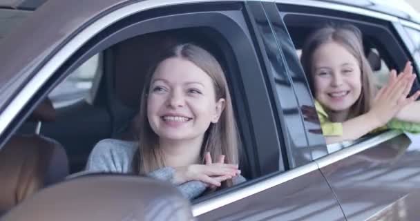 Hermosa mujer joven y niña sentada en el coche en el showroom y aplaudiendo las manos. Emocionados madre e hija eligiendo el vehículo en la concesionaria. Sede del cine 4k ProRes . — Vídeos de Stock