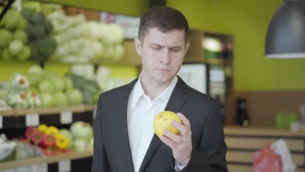 Egy magabiztos, komoly férfi portréja, aki körtét választ a szupermarketben. A fiatal kaukázusi srác sárga gyümölcsöt választott a boltban. Vitaminok, egészséges táplálkozás, életmód, vegetarianizmus. — Stock videók