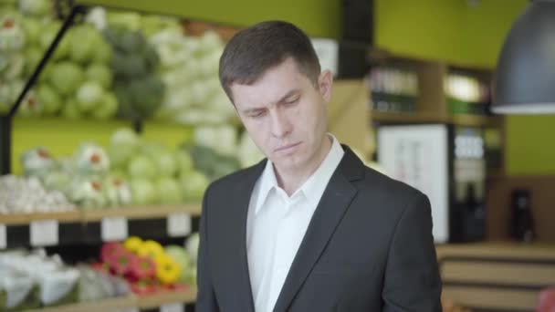 Joven hombre caucásico mirando pera amarilla en la tienda de comestibles y mostrando el pulgar hacia arriba. Tipo seguro de elegir frutas para una dieta saludable en el supermercado y sonriendo. Estilo de vida, alegría, vegetarianismo concepto . — Vídeos de Stock