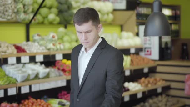 Mittlere Einstellung eines konzentrierten kaukasischen Mannes, der Pomelo im Lebensmittelgeschäft wählt. Porträt eines selbstbewussten jungen Mannes, der gesunde Lebensmittel im Supermarkt kauft. Gesunde Ernährung, Ernährung, Lebensstil. — Stockvideo
