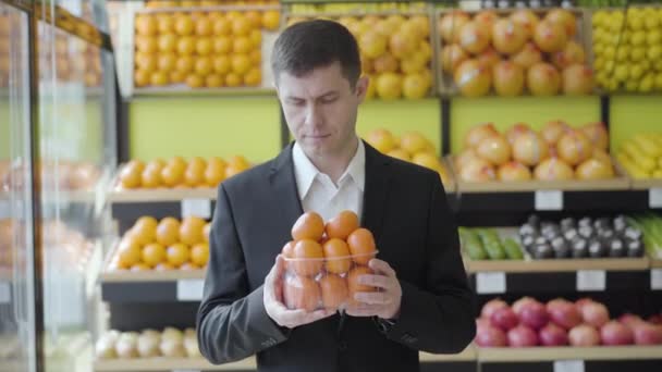 Retrato de cliente de supermercado macho feliz cheirando deliciosas tangerinas frescas e sorrindo para a câmera. Homem caucasiano adulto escolhendo saborosos citrinos de vitaminas na loja de varejo. Estilo de vida, alimentação saudável . — Vídeo de Stock