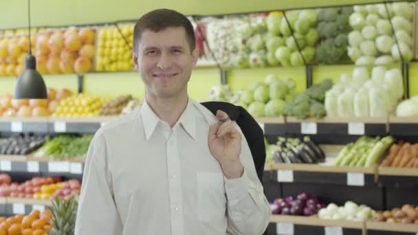 Retrato de joven y alegre moreno caucásico con ojos marrones posando en el supermercado. Hombre adulto feliz en camisa blanca sonriendo a la cámara en el supermercado. Alegría, estilo de vida, concepto de consumismo . — Vídeos de Stock