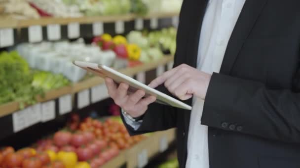 Primer plano de manos caucásicas masculinas usando tableta en tienda de comestibles. Hombre adulto irreconocible en traje usando la lista de compras en la tienda minorista. Estilo de vida, perfeccionismo, compras, consumismo . — Vídeos de Stock