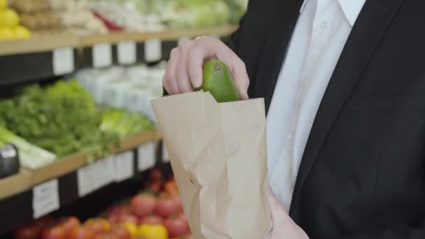 Hombre caucásico desconocido en traje que pone pomelo en el paquete de compras de papel y se va. Un tipo irreconocible comprando sabrosas frutas saludables en el supermercado. Alimentación saludable, estilo de vida, vegetarianismo, dieta . — Vídeos de Stock