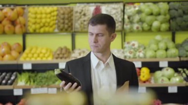 Bakkalda patlıcan seçen ve sebze paketine koyan kendine güvenen genç beyaz adamın portresi. Perakende mağazasında kahverengi gözlü yakışıklı esmer adam. Yaşam tarzı, tüketim.