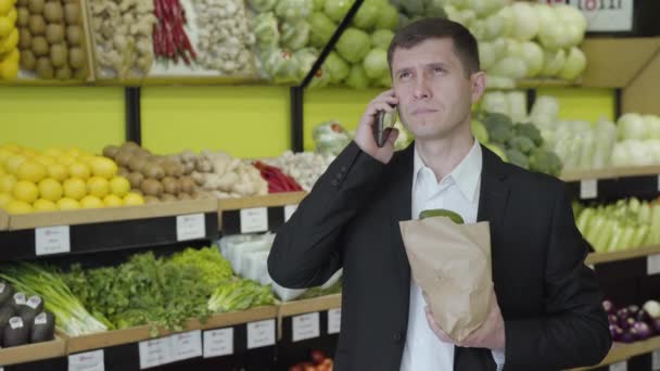 Jonge serieuze blanke man die de telefoon ophangt in de supermarkt en zucht. Zelfverzekerde zakenman in contact als het maken van aankopen in de supermarkt. Lifestyle, rijkdom, zaken, consumentisme. — Stockvideo