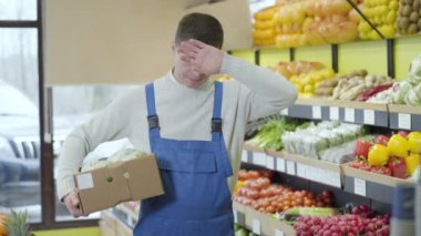 Kafkasyalı yorgun bir adam, alnını eliyle siliyor, iç çekiyor ve lahana kutusuyla gidiyor. Süpermarkette çalışan bitkin bir market çalışanının portresi. Yaşam tarzı, perakende, meslek, ticaret.