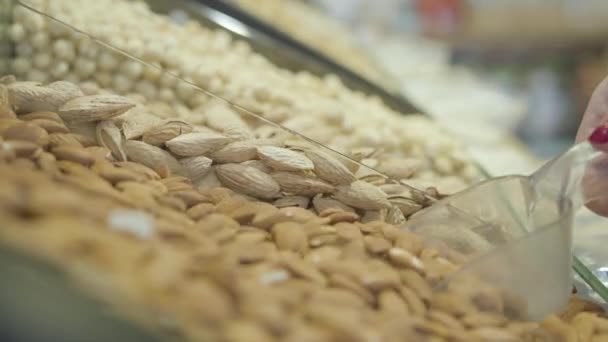 Mano de mujer caucásica irreconocible tomando nueces saludables de la estantería de comestibles. Cliente femenino desconocido recogiendo almendras crudas en el supermercado. Alimentación saludable, estilo de vida, vegetarianismo . — Vídeos de Stock