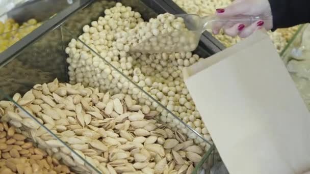 Vrouwelijke blanke hand plukt rauwe biologische macadamia in papieren verpakking. Onbekende vrouwelijke klant die gezonde noten uit de supermarkt haalt. Vegetarisme, gezond eten, levensstijl. — Stockvideo