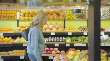 Bakkalda sıra sıra yürüyen ve sohbet eden iki sarışın Kafkasyalı ev kadınının yan görüntüsü. Kendine güvenen ciddi kadınlar süpermarkette sağlıklı yiyecekler seçiyor. Yaşam tarzı, tüketim, satın alma.