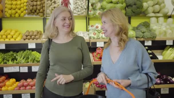 Mujeres adultas caucásicas positivas hablando y riendo en la tienda de comestibles. Rubia amas de casa charlando como compras en la tienda al por menor. Estilo de vida, alegría, consumismo, alimentación saludable . — Vídeo de stock