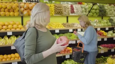 Olgun beyaz bir kadının portresi. Arkadaşına sulu organik nar almasını tavsiye ediyor. Ciddi ev kadınları marketten meyve ve sebze alıyor. Sağlıklı gıda, yaşam tarzı, ticaret.
