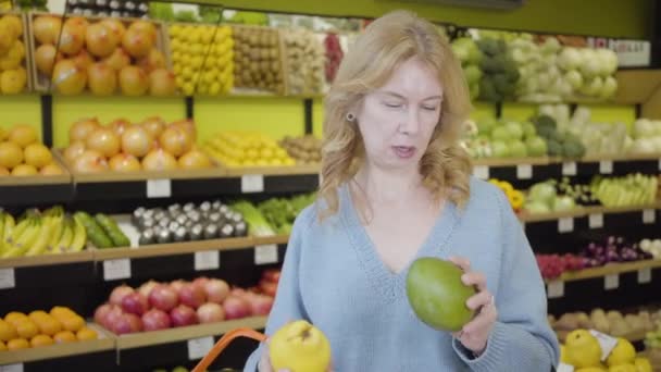 Retrato de una mujer mayor caucásica seria eligiendo frutas en la tienda de comestibles como su amiga que viene con jugosa mandarina y pera. Amas de casa comprando comida orgánica en el supermercado . — Vídeos de Stock