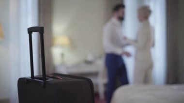 Arka planda bulanık erkek ve kadının kucaklaştığı seyahat çantasının yakın çekimi. Otel odasında buluşan Kafkasyalı genç bir çift. Aşk, eğlence, seyahat, neşe, yaşam tarzı..