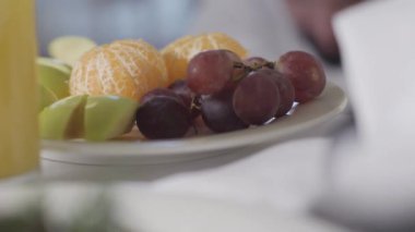 Masanın üzerinde meyvelerle yakın plan beyaz bir kadının bir üzümünü tutması gibi. Tanınmayan bir kadın sabahları sağlıklı taze vitamin yiyecekler yiyor. Boş zaman, yaşam tarzı, vejetaryenlik..