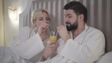 Mutlu beyaz erkek ve kadının portresi bir bardaktan portakal suyu içiyor. Mutlu aşıklar birbirlerine bakıp gülümsüyorlar. Oteldeki lüks otel odasında dinlenen çift. Yaşam tarzı, turizm.