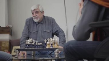 Utanmış beyaz bir adamın portresi satranç masasının önünde oturuyor ve gülümsüyor. Huzurevindeki bir arkadaşla oynayan yaşlı bir emekli..