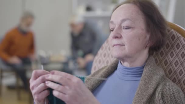 El primer plano de la cara de la mujer caucásica de edad grave tejiendo en sillón. Retrato de una anciana jubilada pasando la noche tranquila en un asilo de ancianos . — Vídeos de Stock