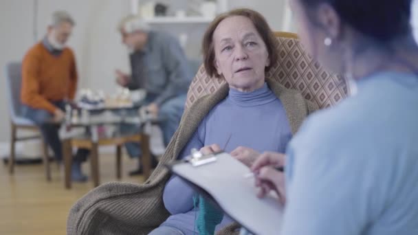 Sorridente donna caucasica matura a maglia e gesticolando sì scuotendo la testa come volontario facendo le sue domande. Felice vecchio pensionato discutendo dieta in casa di cura . — Video Stock