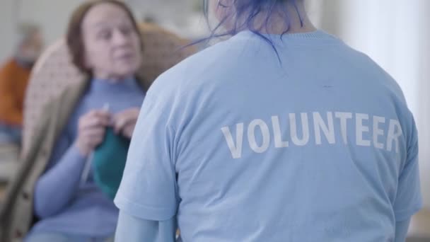 Onherkenbare blanke vrijwilliger praat met wazige oude vrouw in verpleeghuis. Achteraanzicht van jong meisje vrijwilligerswerk en chatten met gepensioneerde. — Stockvideo