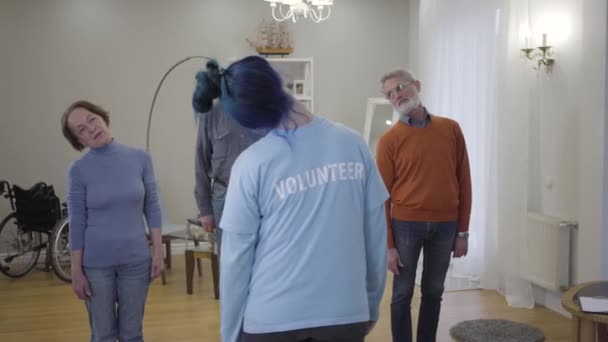 Oudere blanke mannen en vrouwen die 's ochtends oefeningen doen met vrijwilligers. Fysiotherapie van volwassen gepensioneerden in het verpleeghuis. — Stockvideo
