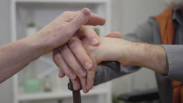 Close-up van oude vrouwelijke blanke handen geplaatst op mannelijke armen met wandelstok. Oudere gepensioneerden steunen elkaar. Lifestyle, ouder worden, eenheid. — Stockvideo