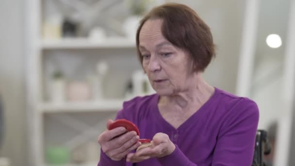 Porträt einer depressiven alten kaukasischen Frau, die mit düsterem Gesichtsausdruck in den Handspiegel blickt. Seniorin erinnert sich an verschwundene Schönheit. — Stockvideo