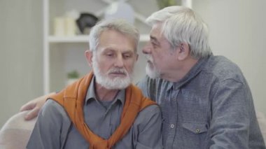 Yetişkin beyaz adamın arkadaşlarının kulağına fıkra fısıldaması. İçeride konuşan ve gülen neşeli emeklilerin portresi..