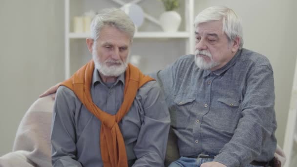 Hombre atento y viejo caucásico apoyando a un viejo amigo. Desesperado triste jubilado compartiendo problemas con un compañero en un asilo de ancianos. Cuidado, estilo de vida, amistad . — Vídeos de Stock