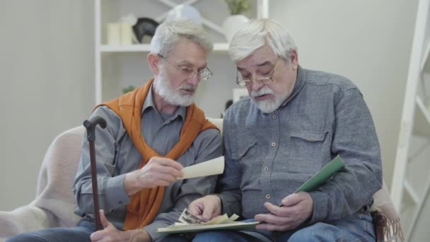 Retrato de homens idosos caucasianos assistindo fotos em preto e branco dentro de casa. Sénior masculino aposentado amigos compartilhando memórias em casa de repouso . — Vídeo de Stock