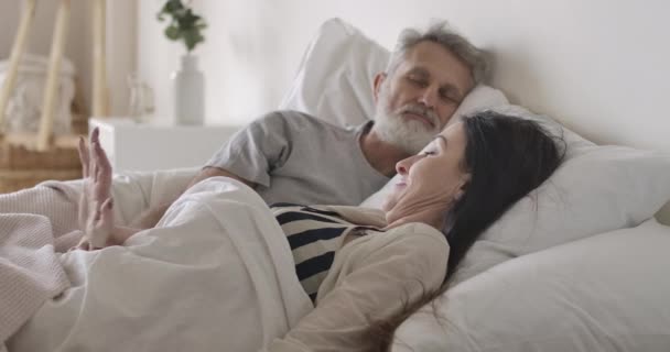 Sidovy närbild av kaukasiska kvinna sträcker sig på morgonen i sängen, sovande make kramar härlig fru. Glad äldre familj vilar på helgerna hemma. Kärlek, livsstil, glädje. Bio 4k ProRes HQ — Stockvideo