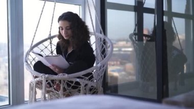 Elinde kitapla koltukta oturan gülümseyen genç bir kadın. Edebiyata düşkün zeki bir kızın portresi. Balkonda gülümseyen ve pencereden dışarı bakan..